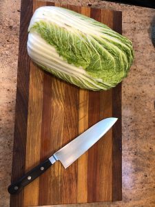whole napa cabbage and chef's knife on cutting board