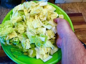 Large bowl of cut cabbage being mixed with salt by hand