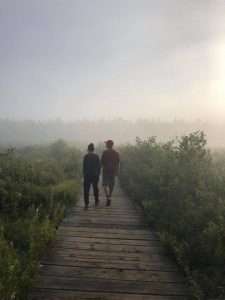 two hikers walking on a boardwalk in the mist
