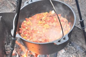 Dutch oven full of stew hanging on tripod over fire