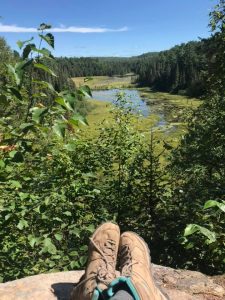 view overlooking beaver pond with crossed legs and hiking boots in shot