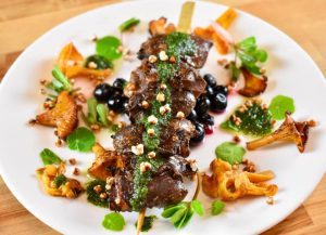 seared goose hearts on a skewer, surrounded by chanterelle mushrooms and green garnishes