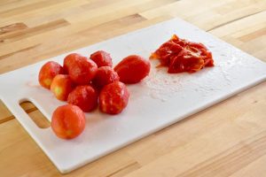 a pile of peeled tomatoes next to a pile of their skins