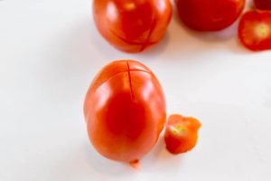 plum tomato with the stem end cut off and a shallow x cut into the bottom