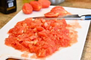 a knife dicing peeled tomatoes on a cutting board