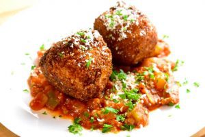 two arancini balls in a bed of red tomato sauce and sprinkled with parmesan