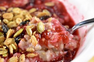 bowl of oatmeal with pink stewed plums topped with granola
