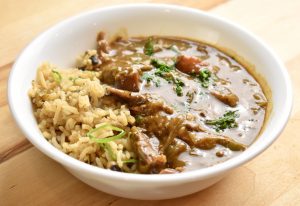 dark goose leg gumbo and dirty rice in a white bowl scattered with parsley