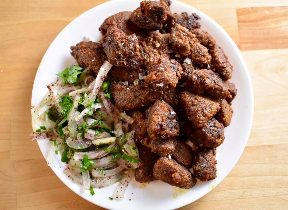 fried cubes of liver on a plate with a raw onion and parsley salad